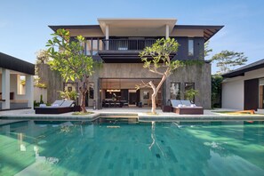 Une maison moderne à deux étages dotée d’une piscine, d’un espace salon extérieur et d’un balcon.