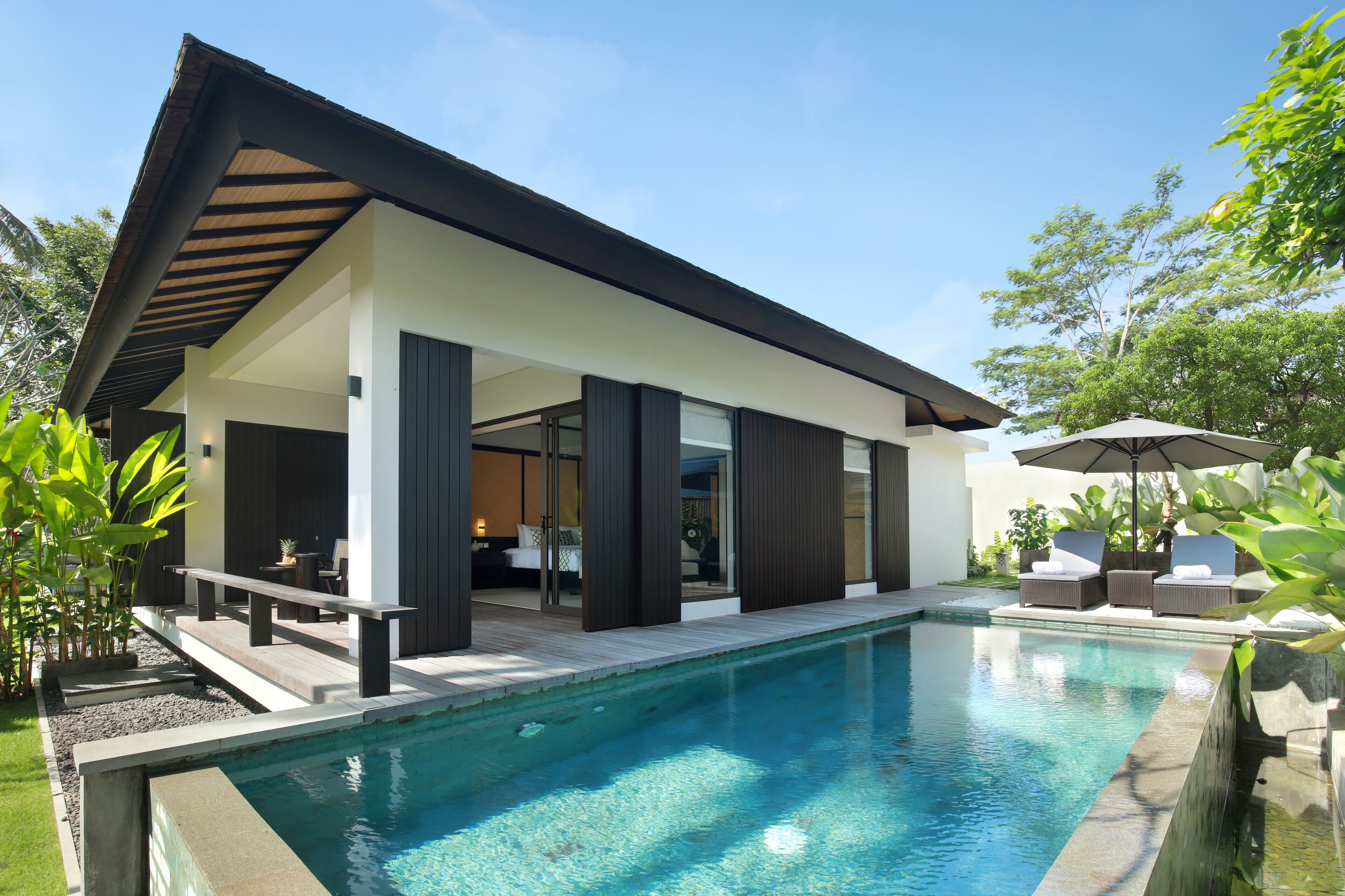 Een modern huis met een zwembad, met een overdekt terras, zitplaatsen en uitzicht op het interieur.