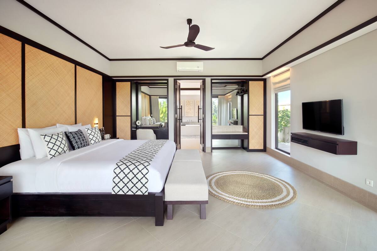 A modern bedroom with a large bed, a ceiling fan, a TV, and a view of the outdoors.