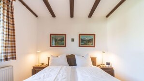 Una cama doble con sábanas blancas, dos mesitas de noche con lámparas y dos cuadros de paisajes en la pared.