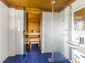 Ein modernes Badezimmer mit einer Holzbank, einer Duschkabine aus Glas und einem weißen Waschbecken mit Tür aus Frostglas.