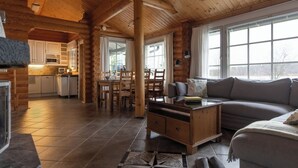 Interior de una cabaña de troncos con comedor, cocina y sala de estar.
