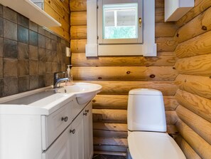 Ein kleines Badezimmer mit Waschbecken, Wasserhahn und Toilette, umgeben von Holzwänden und einem Fenster.
