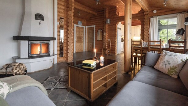 Interior acogedor de una cabaña de troncos, con chimenea, muebles de madera y zona de comedor.