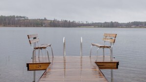 Un muelle de madera que se adentra en un lago tranquilo, con dos bancos uno frente al otro.