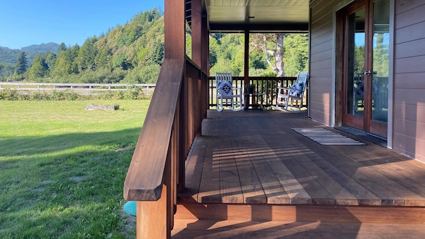 Una terraza de madera con mecedoras y un vidrio que da a un espacio cubierto.
