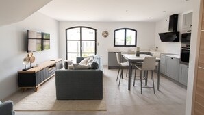 Een moderne keuken met een eethoek, een grijze bank en een aan de muur bevestigde televisie.