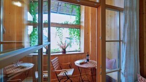 A wooden interior with a dining area, a window with greenery, and a view of the outdoors. - Ferienwohnung Obstgarten, 47 qm 1. Stock, 1 Separates Schlafzimmer (Höslwang)