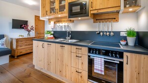 A modern kitchen with wooden cabinets, a built-in microwave, and a stainless steel sink. - Ferienwohnung Obstgarten, 47 qm 1. Stock, 1 Separates Schlafzimmer (Höslwang)