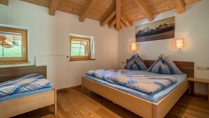 A bedroom with a wooden ceiling, a large bed with blue and white bedding, two bedside tables, a window with blinds, and a radiator. - Very attractive and well cared for apartment (Maria Alm)