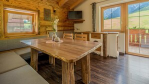 A wooden interior with a dining table, chairs, a TV, and large windows offering a mountain view. - Very attractive and well cared for apartment (Maria Alm)
