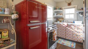 Une cuisine avec un réfrigérateur Galanz rouge, une cuisinière et un pare-feu orné de motifs floraux.