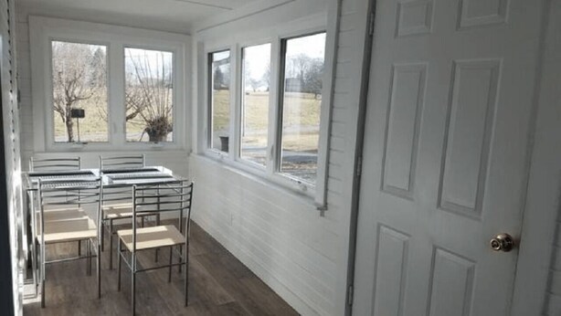 A room with a white door, a window with a view of a field, and a metal bench with a table. - Unity House (Golconda)
