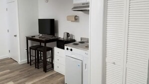 A compact kitchen with a stove, a small refrigerator, and a countertop with a kettle. - Unity House (Golconda)