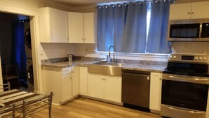 A modern kitchen with white cabinets, a stainless steel sink, a dishwasher, a stove, and a microwave. - Unity House (Golconda)
