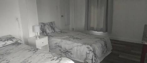 A bedroom with two beds, a nightstand, and a window with curtains.