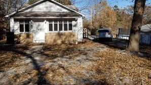 A small, single-story building with a garage, surrounded by trees and a parked car. - Unity House (Golconda)