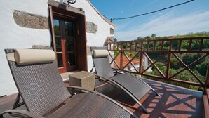 A balcony with wicker chairs, a small table, and a wooden door. - Finca Casa Nanita B (Moya)