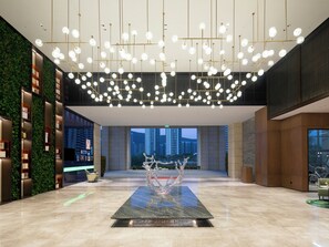 A spacious lobby with a modern chandelier, a central sculpture, and a view of tall buildings. - Hampton BY Hilton Sanya Weiming Lake (SANYA)