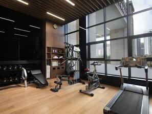 A gym with exercise equipment, a treadmill, and a large window with a city view. - Hampton BY Hilton Sanya Weiming Lake (SANYA)