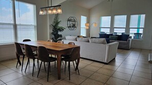 A spacious living room with a dining area, large windows, and a modern chandelier. - Beautiful Bayfront Retreat with Unbeatable Bay and Gulf Views (Bolivar Peninsula)