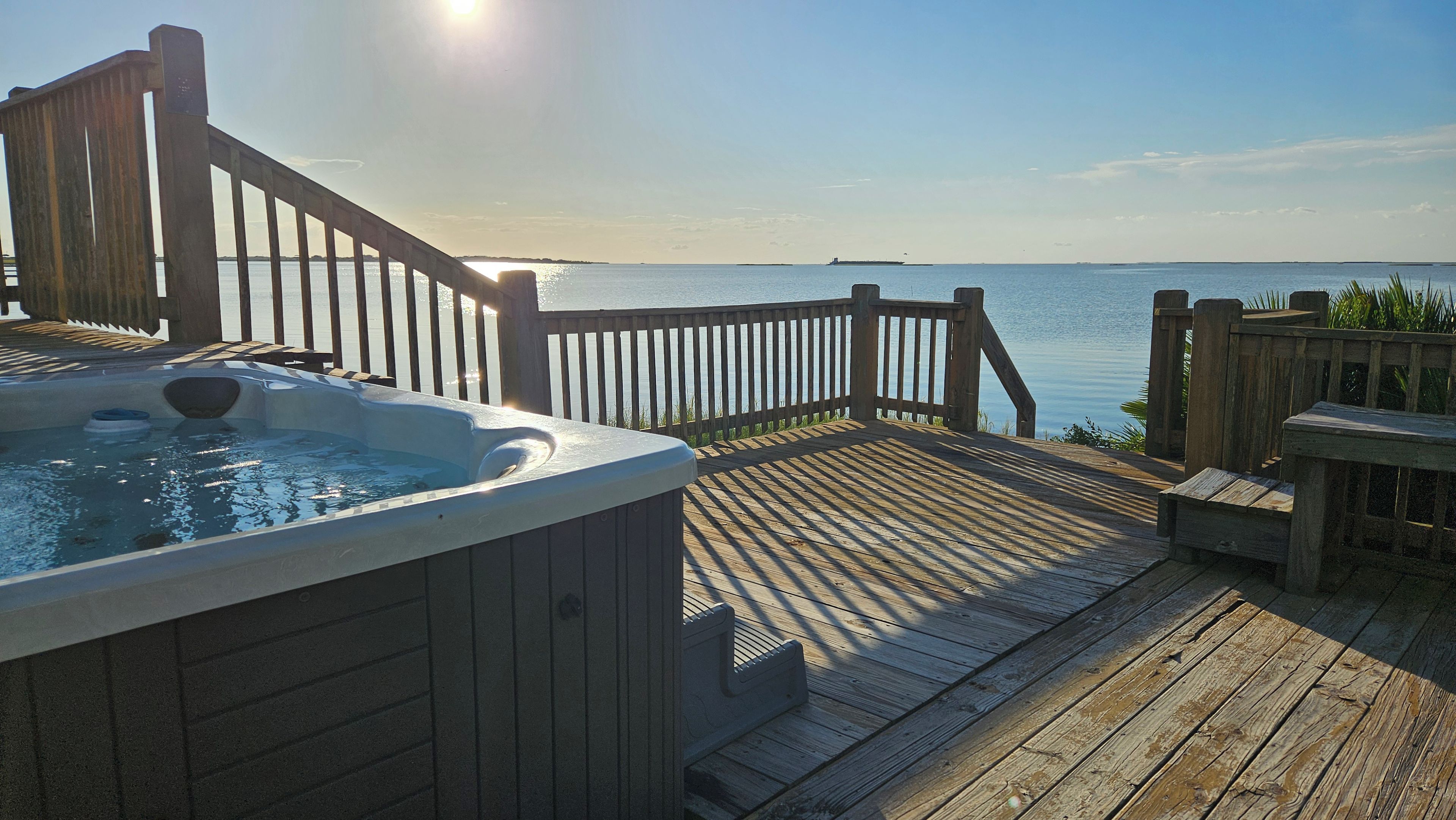Eine Holzterrasse mit Whirlpool und Blick auf das Wasser.