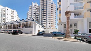 Un edificio moderno con diversi balconi, un'area parcheggio con auto e una palma distintiva.
