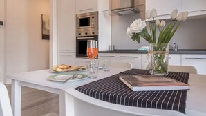 Eine moderne Küche mit weißen Schränken, einem eingebauten Backofen und einer Glasvase mit weißen Blumen auf dem Esstisch.