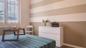 Ein Schlafzimmer mit einem Bett, einem Schminktisch, einem Stuhl, einem Tisch mit Tablett und einem Fenster mit Jalousien.