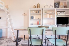 A room with a bunk bed, a desk with a chair, a television, and shelves with decorative items.