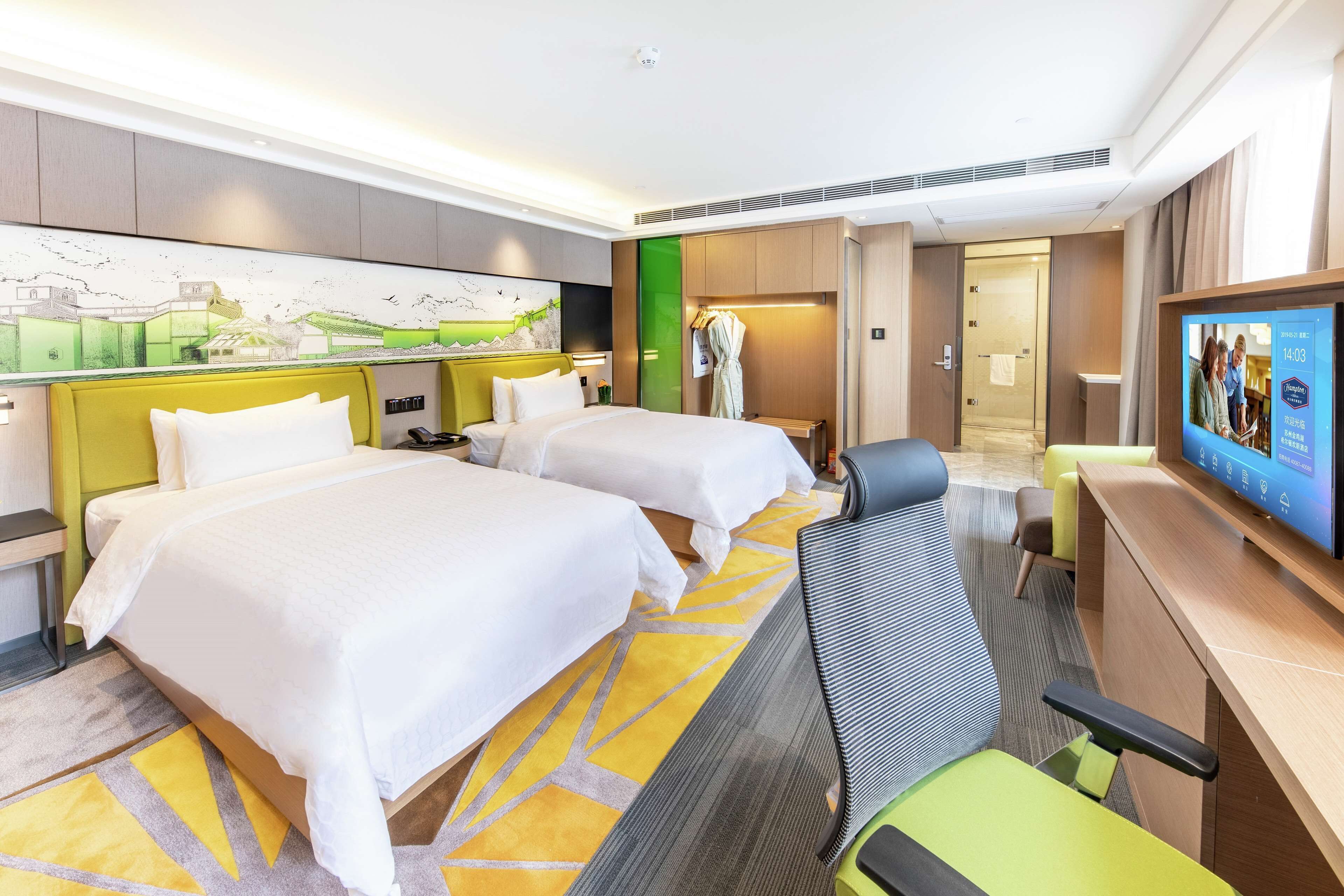 A hotel room with two beds, a desk, a television, and a painting on the wall.
