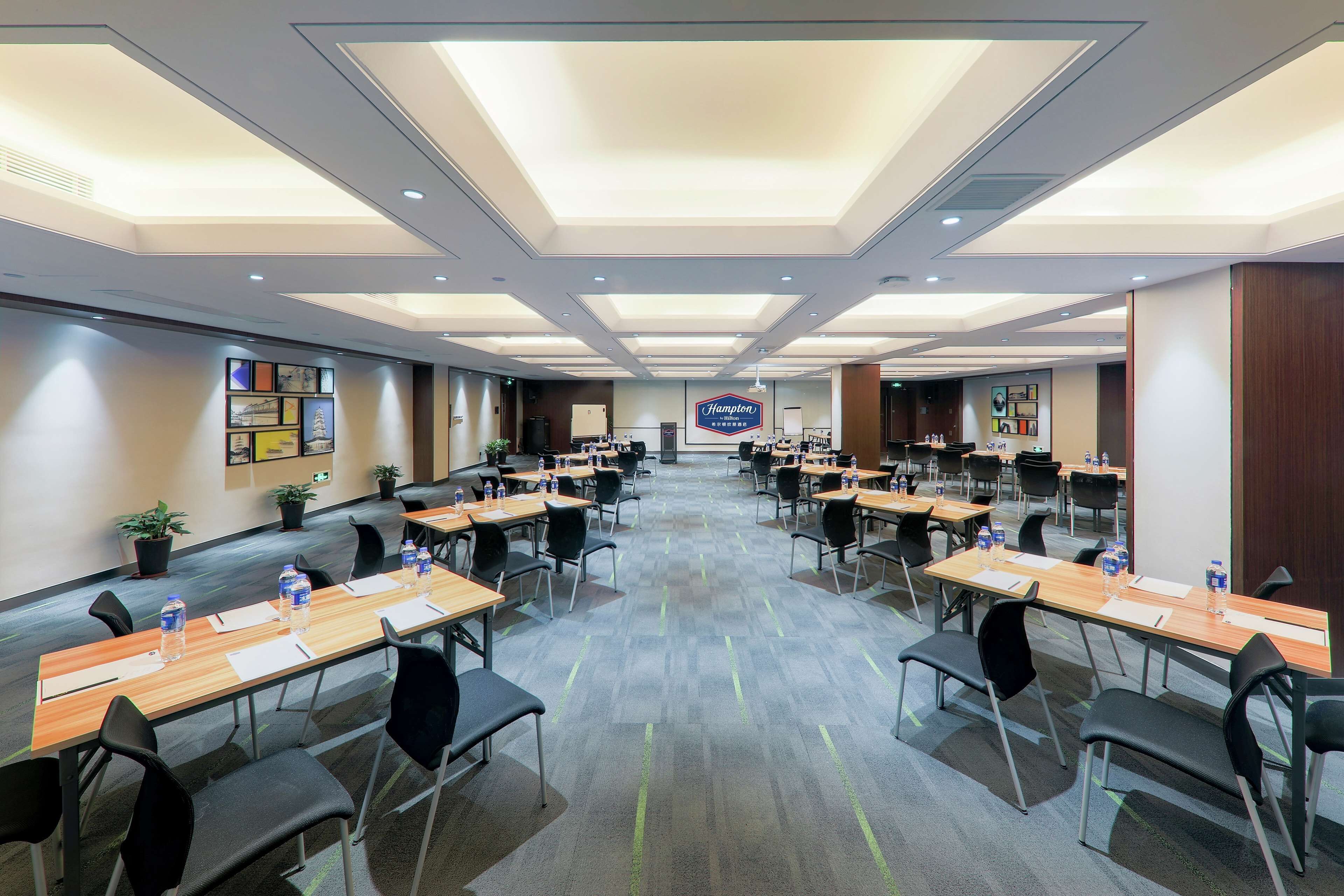 Ein Hotelkonferenzraum mit mehreren Tischen und Stühlen, einem großen Hampton-Schild und einem modernen Deckenstil.