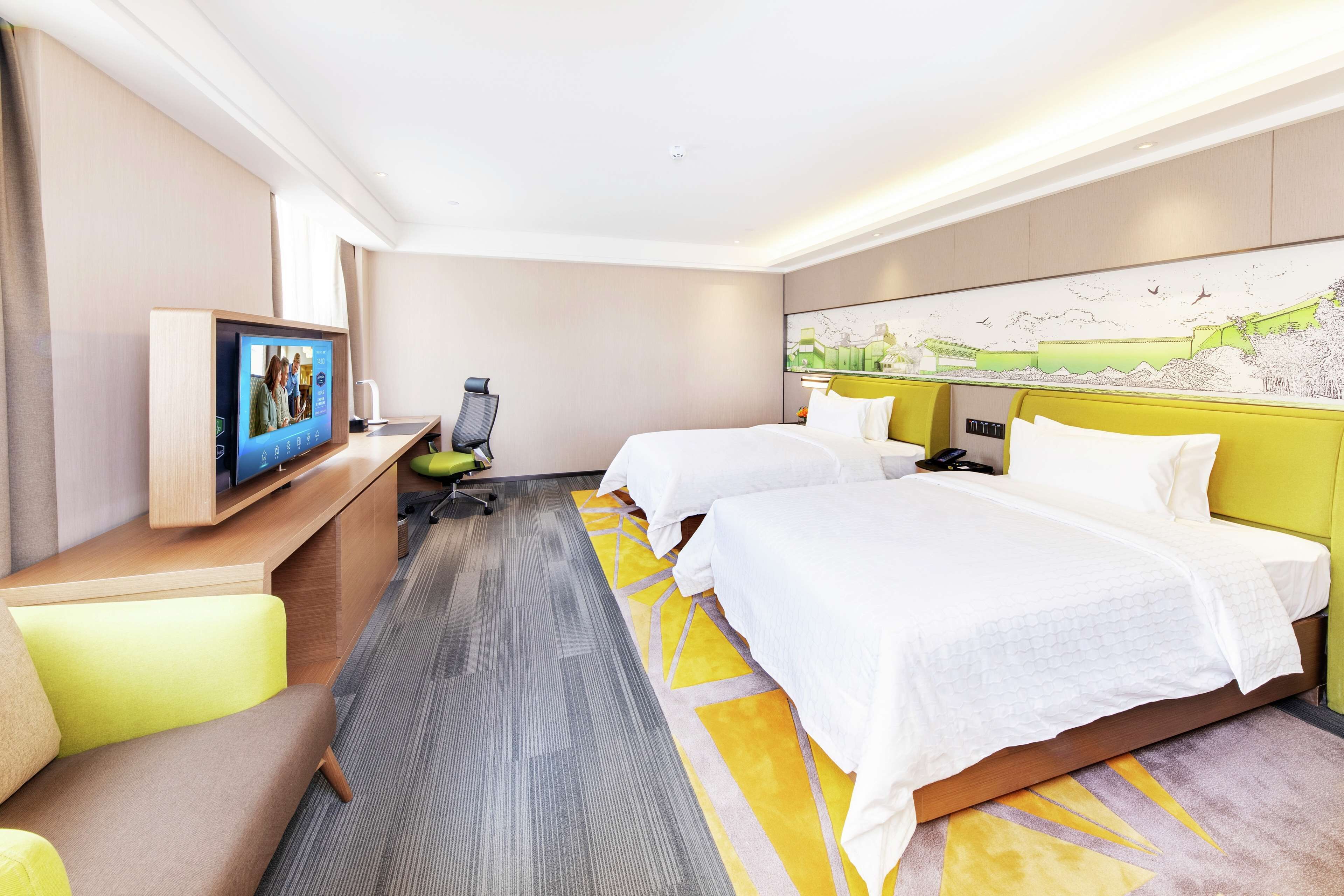 A hotel room with two beds, a desk with a computer, a chair, and a large painting on the wall.