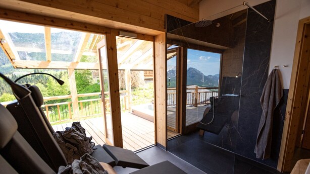 Un bagno moderno con uno specchio grande, soffitto in legno e vista su una terrazza e montagne.