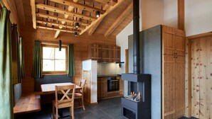 L’intérieur chaleureux d’un chalet avec un coin repas en bois, un poêle encastré et une cuisine dotée de meubles en bois.
