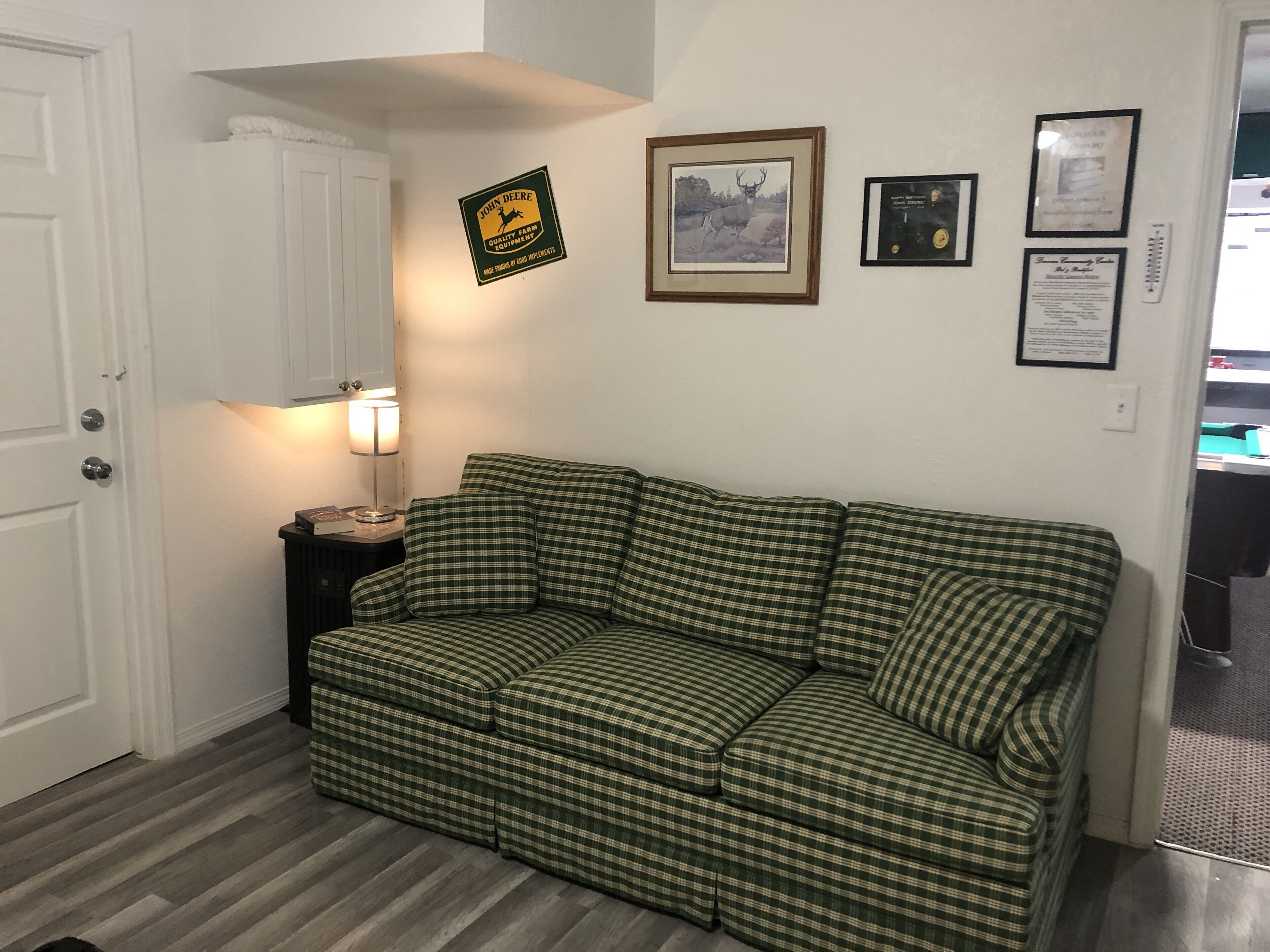 Ein Zimmer mit einem grün karierten Sofa, einer Lampe auf einem Beistelltisch und Wanddekorationen, darunter ein gerahmtes Bild und Zeugnisse.