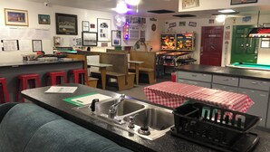 Une cuisine avec un coin bar, une table de billard et une porte rouge portant l’inscription « FUMER INTERDIT ».