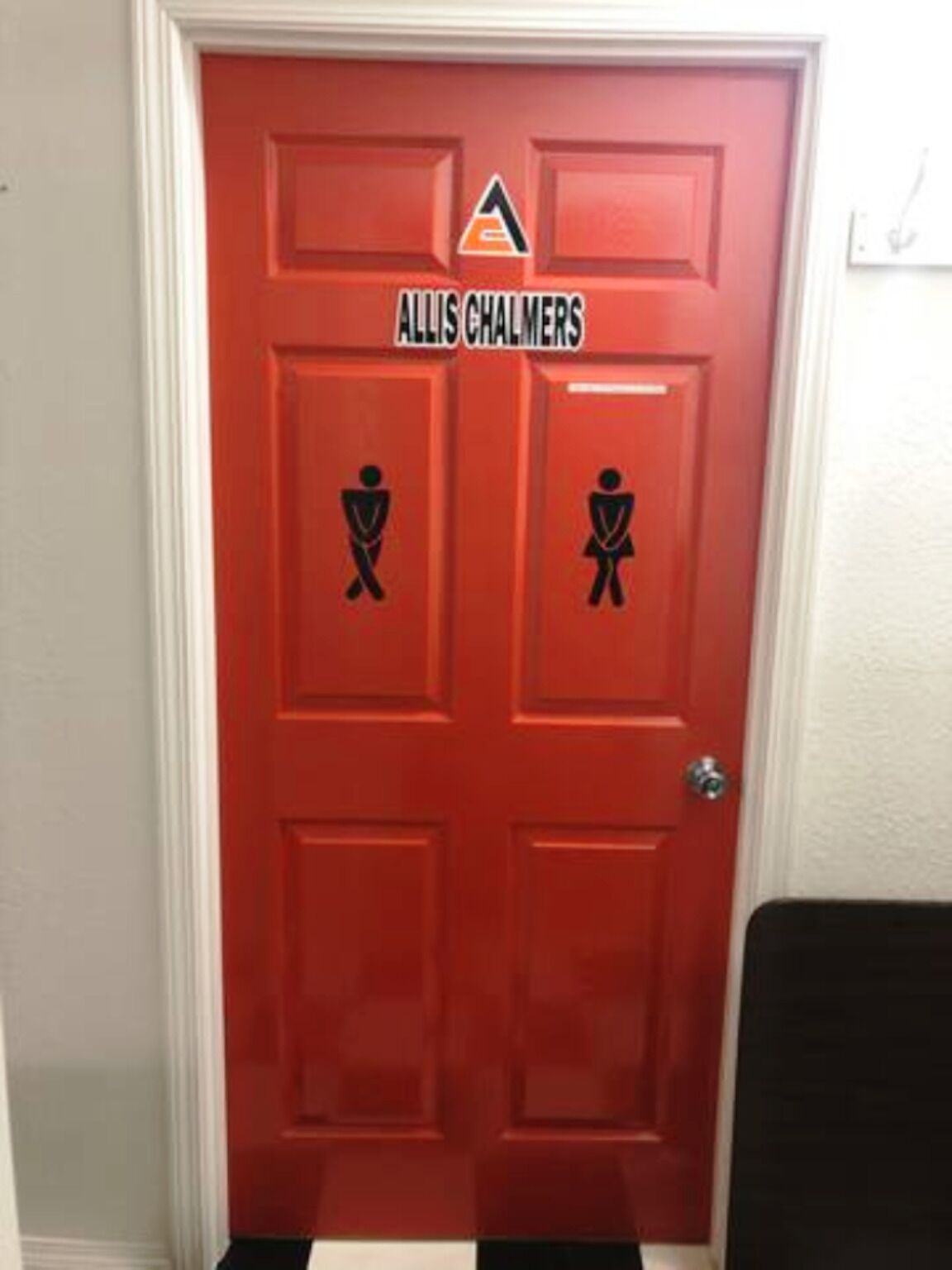 A red door with the name "ALLIS CHALMERS" and two restroom symbols.