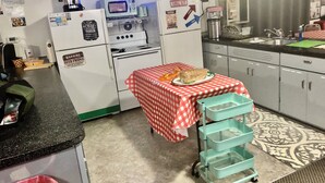 Une cuisine compacte équipée d’un four à micro-ondes, d’une cuisinière et d’un réfrigérateur. Une table recouverte d’une nappe à carreaux et sur laquelle est posé un pain se trouve au centre de la pièce.