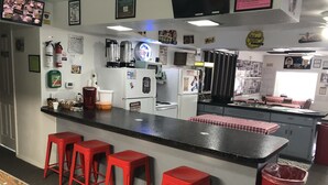 Une cuisine avec un coin bar, des tabourets rouges, une table de billard et divers appareils électroménagers.