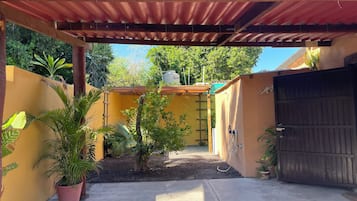 Un patio couvert doté d’un sol en béton, de plantes en pot et d’un portail en métal.