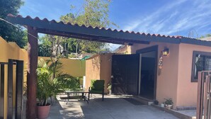 A patio area with a pergola, a table, and chairs, surrounded by a yellow wall and a gate. - Cozy and comfy little house in the heart of Loreto (Loreto)