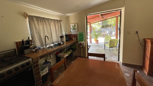 A kitchen with a stove, sink, and a dining table. There is a window with curtains and a view of the outside. - Cozy and comfy little house in the heart of Loreto (Loreto)