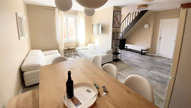 A modern living room with a wooden dining table, white sofas, and a staircase leading to a loft area. - Villa Alexandra (Le Crotoy)
