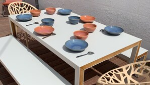 A dining table with multiple bowls and spoons, surrounded by chairs and a bench on a wooden deck. - Villa Alexandra (Le Crotoy)