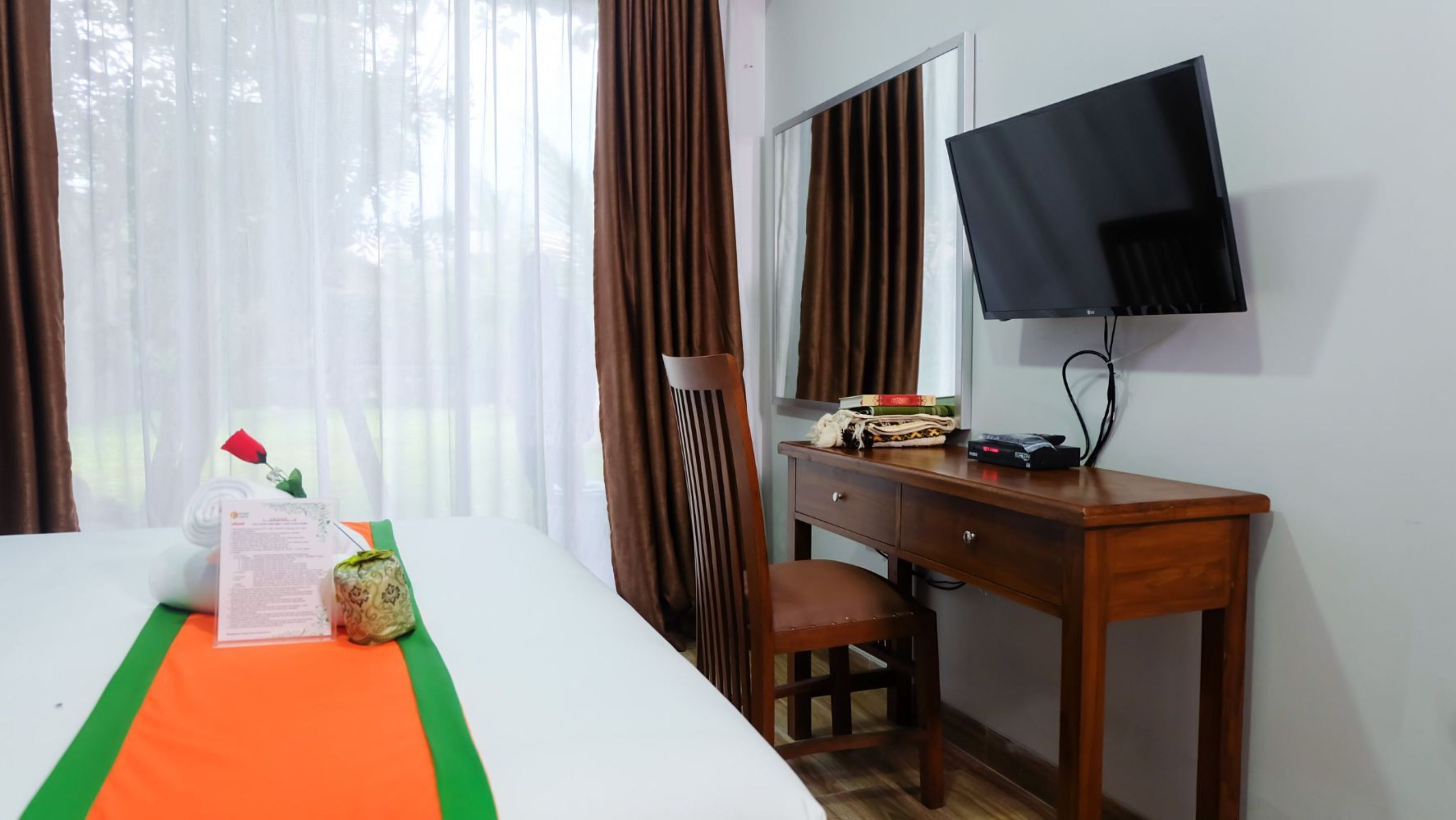 A hotel room with a bed, a desk, a chair, a television, and a window with curtains.