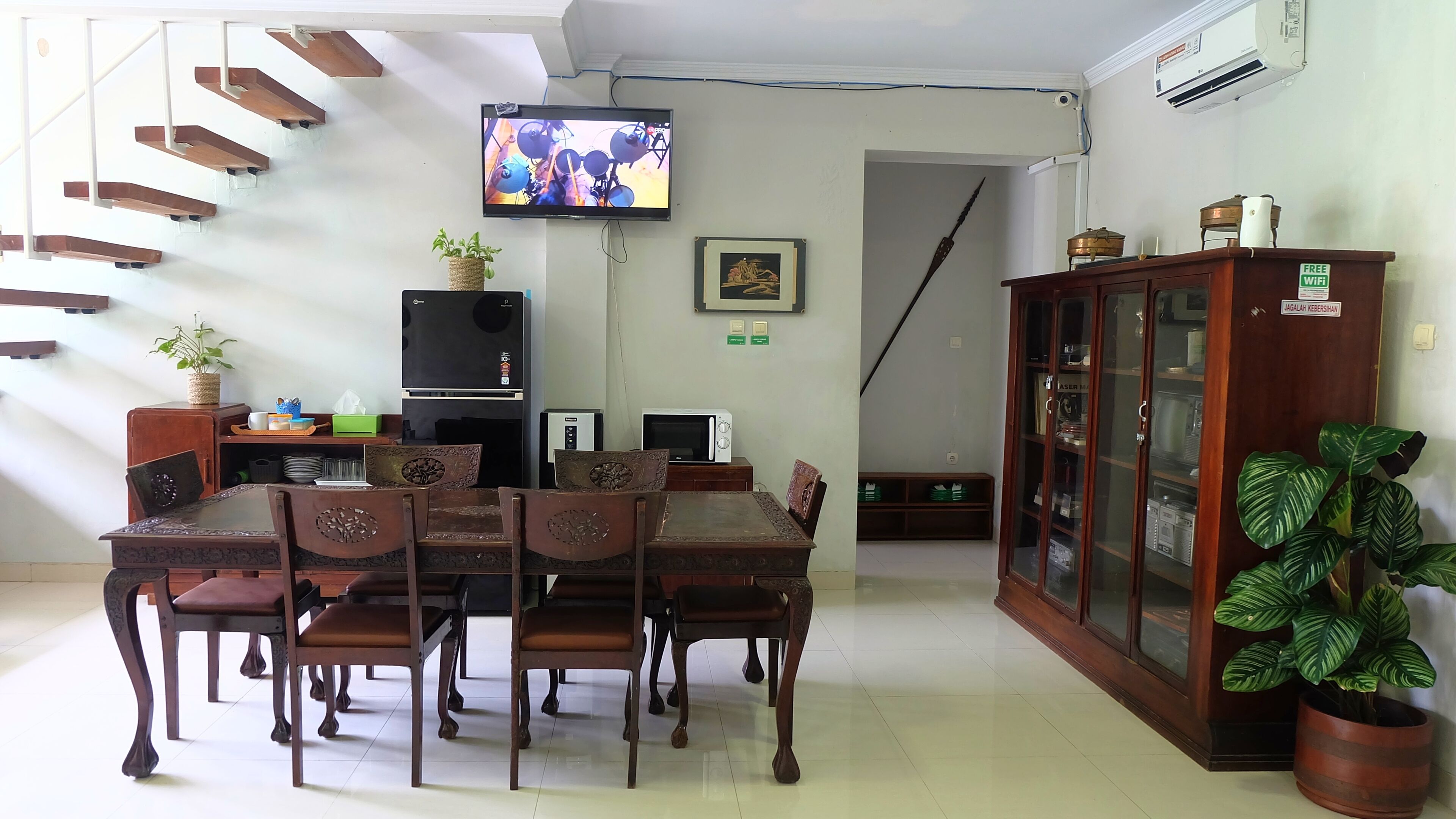A dining area with a wooden table and chairs, a television mounted on the wall, and a cabinet with glass doors.