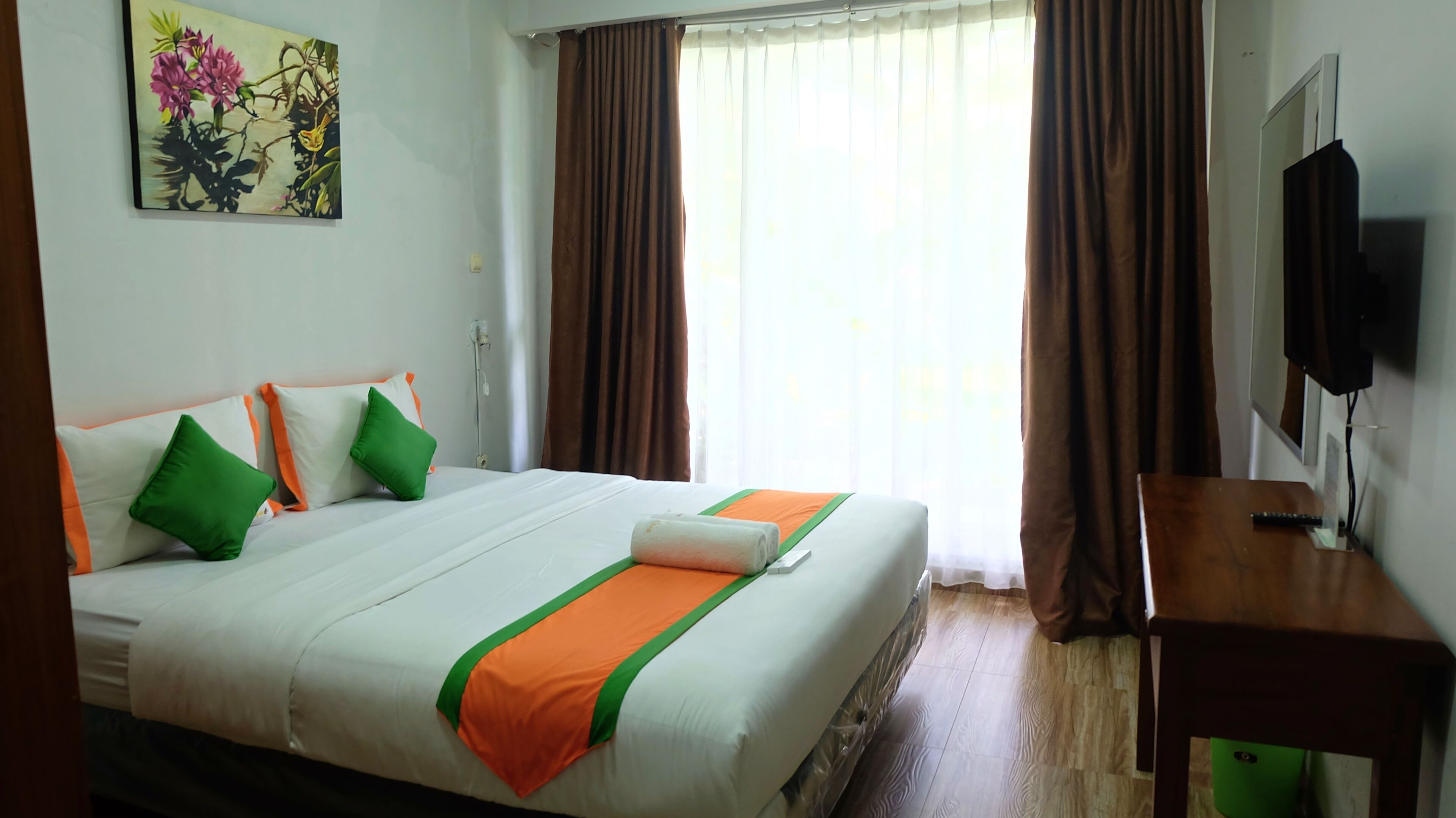 A hotel room with a large bed, a television, and a painting on the wall.