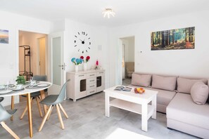 Een moderne woonkamer met een eethoek, een bank, een bijzettafeltje, een klok en een schilderij aan de muur.