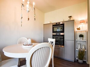 A compact kitchen with a built-in oven, a white dining table with two chairs, and a hanging light fixture.